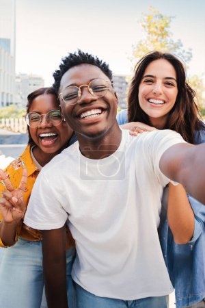 Téléchargez les photos : Portrait vertical d'un groupe de jeunes étudiants multiraciaux souriant prenant un selfie ensemble. Heureux adolescent afro-américain riant avec ses amis gais. Des camarades de classe en réunion amicale - en image libre de droit