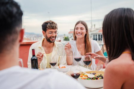 Téléchargez les photos : Joyeux couple de jeunes adultes souriant, riant et dînant avec leurs amis lors d'une fête amicale. Deux membres de la famille qui se nourrissent pour célébrer un barbecue avec leurs copains à la maison - en image libre de droit