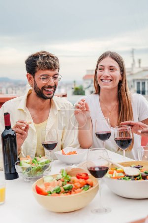 Téléchargez les photos : Portrait vertical d'un couple de jeunes adultes heureux souriant et dînant avec leurs amis lors d'une fête amicale pour le déjeuner. Les membres de la famille qui se nourrissent en célébrant un barbecue avec leurs amis. Haut - en image libre de droit