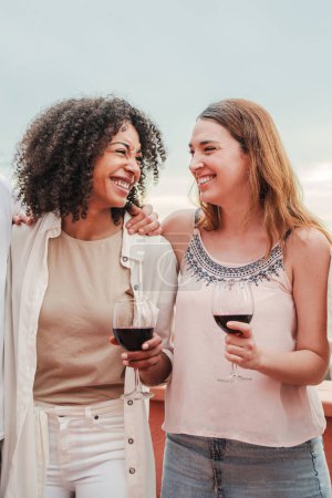 Foto de Retrato vertical de dos amigas jóvenes divirtiéndose hablando y bebiendo vino. Mujeres adultas sonriendo y sosteniendo copas de vino en la celebración de la fiesta. Señoras o niñas sonriendo con gafas de alcohol. Alto. - Imagen libre de derechos