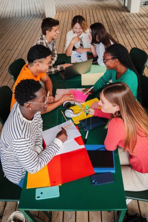 Photo for Vertical high angle view of a big group of multiracial teenage students working on university assignment homework project on high school library. Teamwork of diverse young classmates studying together - Royalty Free Image