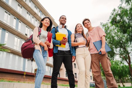 Photo for Portrait of a group of smiling multiracial university students carrying backpacks and folders, standing at campus. Multiracial young classmates socializing after class. Teenage guys and young ladies - Royalty Free Image