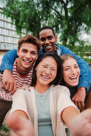 Foto de Retrato vertical de un grupo de jóvenes estudiantes de secundaria multirraciales con una sonrisa dentada tomando una selfie afuera mirando a la cámara, riendo y divirtiéndose juntos. Amistosos adolescentes tomando una foto - Imagen libre de derechos