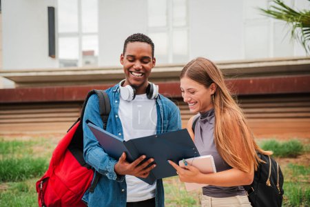 Photo for High school student guy smiling while showing his female colleague the homeworks and the lesson for the exam. Two multiracial friends reading, checking results of a test, talking at university campus - Royalty Free Image