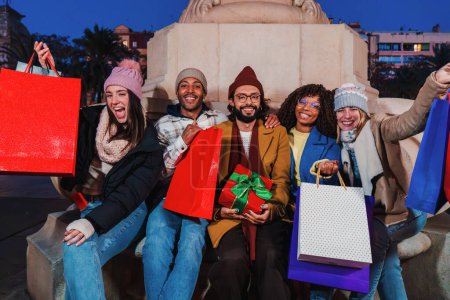 Photo for Group of best friends celebrating the christmas together, showing their shopping bags. Happy people with xmas gifts and presents enjoying a festive night. Buddies purchasing sales at christmastime - Royalty Free Image