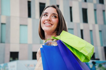 Photo for Portrait of beautiful fashion woman going shopping carrying colorful paper bags walking and looking up with a smiley expression outdoors. Caucasian happy young adult female enjoying sales purchases - Royalty Free Image