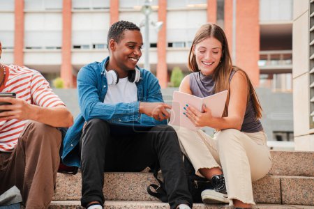 Téléchargez les photos : Deux étudiants adolescents multiraciaux apprenant ensemble sur le campus universitaire. Un écolier afro-américain parlant des devoirs avec une écolière. De jeunes amis étudient dans les escaliers du lycée. Haut - en image libre de droit