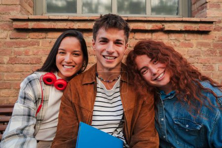 Photo for Group of three real classmates sitting at university campus. Group of young high school students looking at camera. Teenage multiracial people staring front. Adolescent schoolboys at academy break - Royalty Free Image