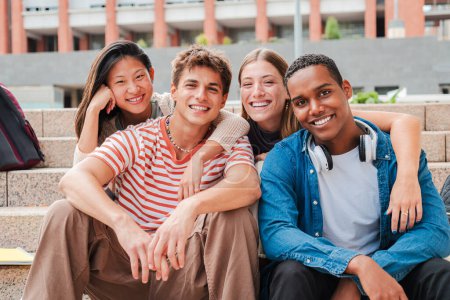 Téléchargez les photos : Portrait d'un groupe de vrais lycéens multiraciaux souriant et regardant une caméra assise sur les marches d'un escalier d'un campus universitaire. Des amis adolescents internationaux rient. Les jeunes - en image libre de droit