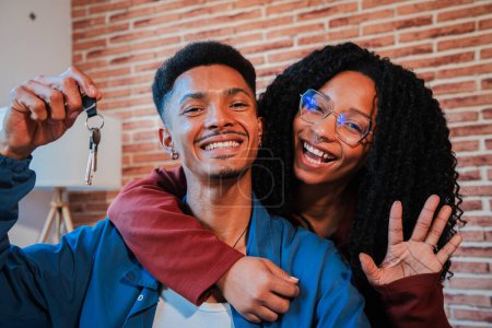 Téléchargez les photos : Jeune couple afro-américain montrant les clés de leur première maison après l'achat et le déménagement dans une nouvelle maison ensemble. mari et femme heureux câlins dans leur appartement excité d'être propriétaires d'un appartement - en image libre de droit