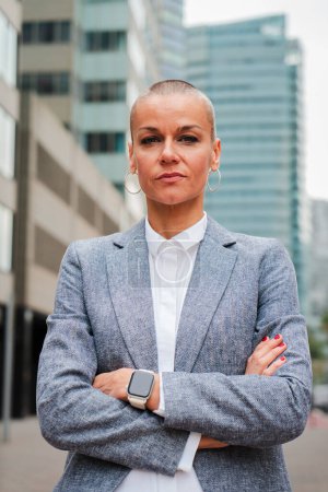 Photo for Vertical individual portrait of a serious arms crossed businesswoman with short hair looking at camera with pensive expression. Lawyer or executive staring front at workplace. Real confident female - Royalty Free Image