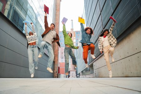 Foto de Grupo de estudiantes adolescentes reales divirtiéndose saltando en el campus universitario. Jóvenes adultos amigos multirraciales saltando en la escuela secundaria. Feliz adolescentes emocionados celebrando después de pasar los exámenes. Objetivo académico - Imagen libre de derechos