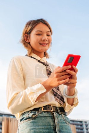 Photo for Vertical teenage chinese woman using her smartphone and chatting online or browsing on internet. Young asian college student lady watching funny videos with a smartphone. Female watching the phone - Royalty Free Image