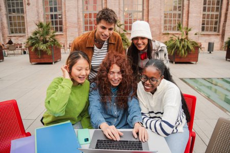 Foto de Un grupo diverso de estudiantes adolescentes alegres se agrupa en el campus universitario, trabajando diligentemente en una tarea usando su computadora portátil, enfocada en recopilar información de la computadora - Imagen libre de derechos