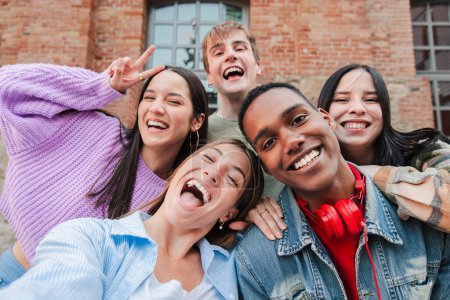 Foto de Grupo de jóvenes estudiantes adultos multirraciales sonriendo y tomando una selfie juntos. Retrato de adolescentes internacionales felices riendo. Amigos alegres divirtiéndose. Compañeros de clase en una reunión amistosa - Imagen libre de derechos
