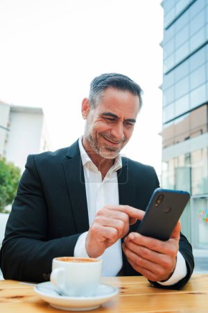 Téléchargez les photos : Portrait vertical d'un homme d'affaires utilisant son téléphone portable à l'extérieur. Homme mature naviguant en ligne avec un appareil de téléphone intelligent. Entrepreneur d'âge moyen souriant et messages texte avec un téléphone portable. Haut - en image libre de droit