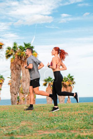 Photo for Vertical. young Caucasian couple running on the beach wearing sportswear. A sporty man and a healthy woman enjoy exercising on the shoreline. Friends having a cardio workout jogging at coast line - Royalty Free Image