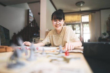 Photo for Role playing tabletop and board game hobby concept. Happy young adult asian woman enjoying with storytelling fantasy adventure. Blur foreground with monster miniatures and dice component. - Royalty Free Image
