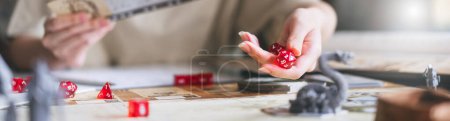 Photo for Role playing tabletop and board game hobby concept. D20 dice roll by people hand for begin narrative adventure story. Blur book and miniatures. Banner size background. - Royalty Free Image