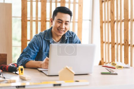 Photo for Middle age adult southeast asian man carpenter job concept. Using laptop for online working with customer. People working from home with techonology concept. - Royalty Free Image
