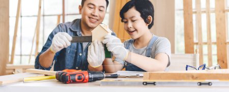 Photo for Focus on wooden house model. Asian family father and son diy or repair at home concept. Dad teach using tools carpenter or engineer education skill with child at workshop. - Royalty Free Image