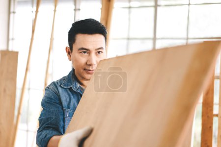 Photo for Middle age adult southeast asian man carpenter job concept. Father holding wooden plank and eye looking forward with confidence. Indoor background at home workshop - Royalty Free Image