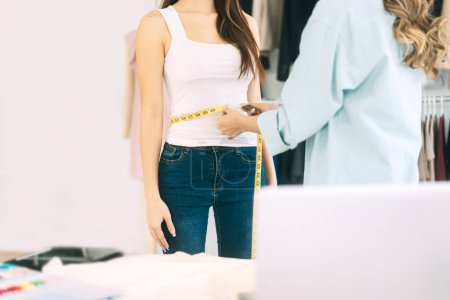 Photo for Two people tailor working in fashion design concept. Young adult asian woman designer using tape measure for size and cutting clothes studio dressmaker. - Royalty Free Image