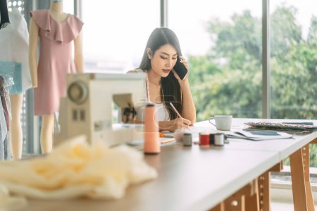 Photo for People tailor work or study in fashion design studio concept. Young adult asian woman designer busy talking with customer. Background with sewing machine and mannequin. - Royalty Free Image
