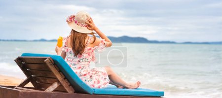 Photo for Summer beach holiday concept. Young asian woman relax on beach hold orange refreshment cocktail with floppy hat in pink dress. Clear sky background banner with copy space. Pattaya, Thailand - Royalty Free Image