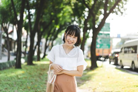 Foto de Young adult business asian woman walking in public park outdoor. People in city after working relax in nature environment for healthy lifestyle. - Imagen libre de derechos