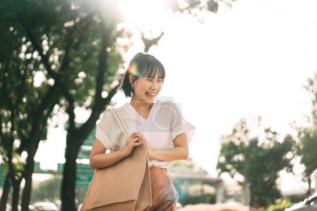 Foto de Feliz sonrisa joven adulto negocio asiático mujer caminando en público parque al aire libre. Personas en la ciudad después de trabajar relajarse en el entorno natural para un estilo de vida saludable. - Imagen libre de derechos