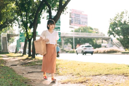 Foto de Joven adulto negocio asiático mujer caminando en sendero al lado de la calle. Personas en la ciudad después de trabajar relajarse en el entorno natural para un estilo de vida saludable. - Imagen libre de derechos