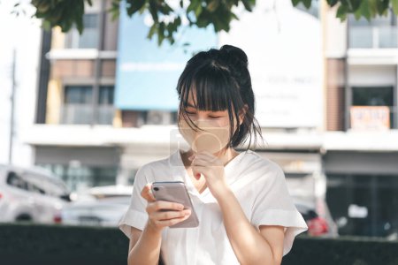 Foto de Young adult business asian working woman wear face mask for protect virus corona or covid19. Using mobile phone application. Urban people lifestyle after got vaccine on day concept. - Imagen libre de derechos