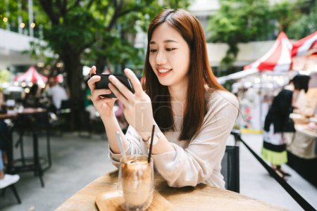 Photo for Happy young asian adult woman casucal city lifestyle on weekend at cafe. Relax at restaurant using smart phone for social media. Outdoor area on day time. Bangkok, Thailand - Royalty Free Image