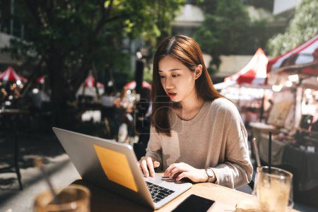 Téléchargez les photos : Entreprise pigiste adulte asiatique femme utilisant un ordinateur portable pour le travail au café trottoir. Joyeux et sourire visage. Style de vie urbain avec la technologie moderne sur le jour. - en image libre de droit