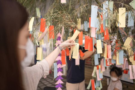 Téléchargez les photos : Tanabata festival de la culture japonaise en juillet été. Vue arrière de la main de la femme tenant la carte de papier de voeu pour accrocher sur le bambou. - en image libre de droit