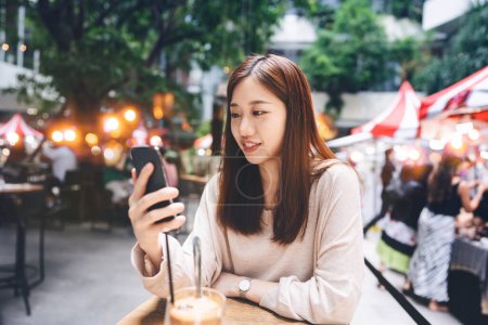 Photo for Young adult asian woman using mobile phone for surfing the net at cafe. People window shopping lifestyle. Background with bokeh light - Royalty Free Image