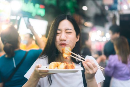Foto de Poeple viajar y comer concepto de comida callejera. Feliz joven adulto asiático foodie mujer holding gyoza en Chinatown Yaowarat mercado, Bangkok, Tailandia. - Imagen libre de derechos
