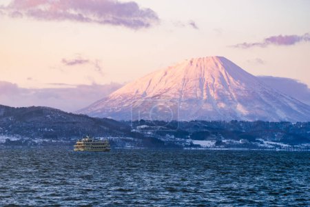 Foto de Lago Toya con barco de turismo en la vista del atardecer en la ciudad de Toyako. Montaña Yotei en el fondo. Hokkaido, Japón. - Imagen libre de derechos
