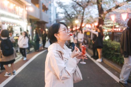 Photo for Japan Tokyo city Nakameguro sakura festival famous destination. Young adult asian woman eating strawberry sparkling wine. Japanese people lifestyles at night street sightseeing. - Royalty Free Image