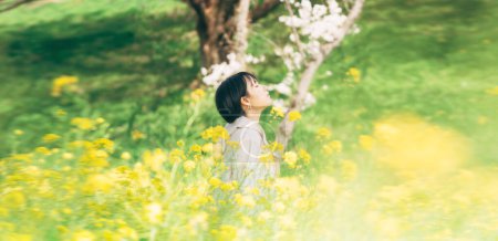 Téléchargez les photos : Jeune femme japonaise asiatique adulte debout se détendre et calme dans le champ de fleur jaune. Loisirs de plein air dans la nature au printemps. - en image libre de droit