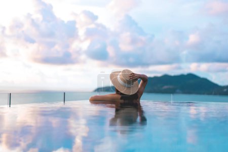 Téléchargez les photos : Voyage d'été en vacances au concept tropical du sud-est. Vue arrière Asie femme se détendre à la piscine de luxe en plein air station balnéaire panorama ciel avec vue sur les nuages. Phuket, Thaïlande - en image libre de droit