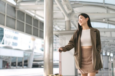 Foto de Mujer asiática adulta joven independiente caminando con equipaje de viaje para viaje de negocios. Hermosa sonrisa cara pelo largo en la plataforma de la estación en el día. Estilos de vida urbanos. - Imagen libre de derechos