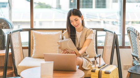 Photo for Business travel people doing freelance digital nomad job concept. Happy smile face young asian woman sitting indoors lounge with laptop and luggage. - Royalty Free Image