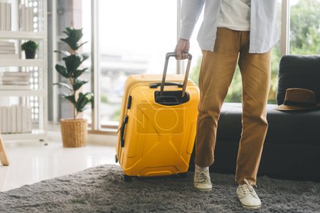 Photo for People getting ready for holidays travel trip concept. Single traveller man walking carry a luggage begin a journey. Men wear casual cloth and sneakers. Background in living room at home or hotel. - Royalty Free Image