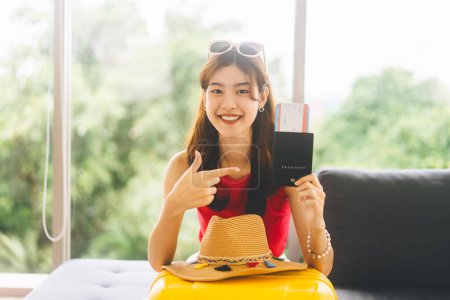 Photo for Portrait of young adult southeast asian woman with yellow travel luggage. People hand holding passport and airplane ticket fo departure boarding. Sitting on sofa at home or hotel. - Royalty Free Image