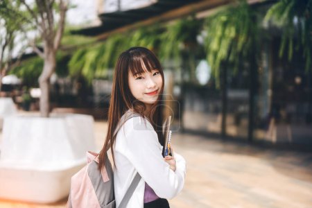 Téléchargez les photos : Collège gens style de vie de la ville sur le concept de jour. Portrait de jeune adulte asiatique étudiante femme. Tenir un carnet et porter un sac à dos à l'extérieur. - en image libre de droit