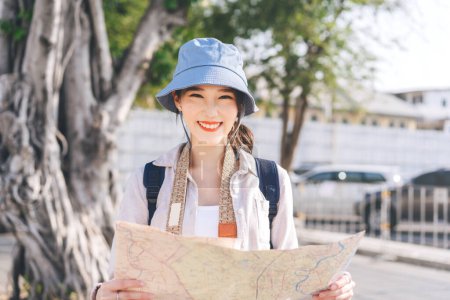Téléchargez les photos : Attrayant jeune hipster adulte voyageur asiatique femme porter chapeau bleu et sac à dos. Recherche de la destination sur le voyage de la ville par carte. Séjour concept voyage d'été. - en image libre de droit