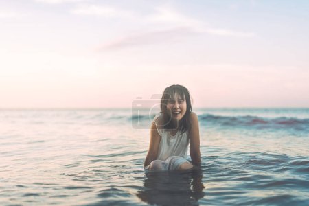 Foto de Retrato de mujer asiática en la playa con el pelo mojado. Sentado en las olas del mar Fondo de luz solar. Estilo de vida al aire libre en concepto de día. - Imagen libre de derechos