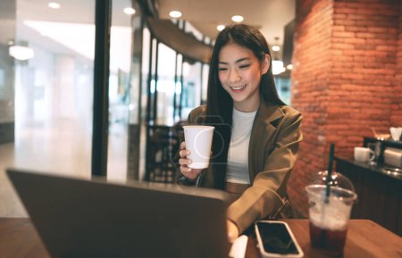 Téléchargez les photos : Entreprise freelance jeune femme asiatique adulte tenant tasse de café au café. Les citadins style de vie pause du travail. Joyeux sourire visage. - en image libre de droit